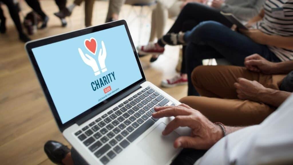 Donasi amal online meperan teknisi ITlalui laptop yang menampilkan logo kegiatan amal dan charity, di aula pertemuan yang penuh peserta, menunjukkan inovasi dalam kegiatan sosial dan pengumpulan dana.